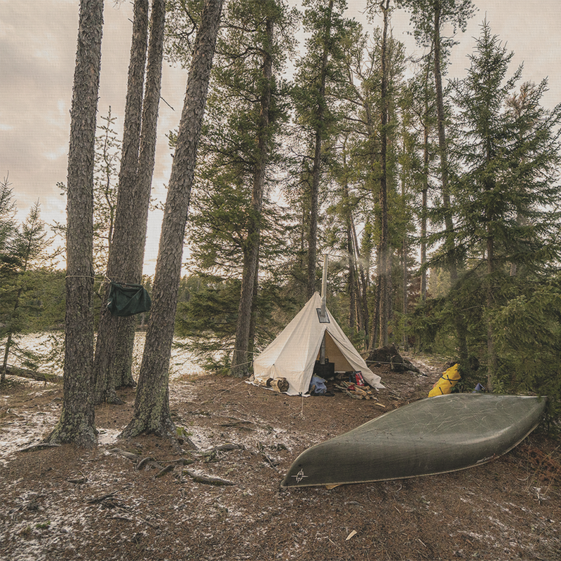 an esker tent, pitched in the woods with a canoe resting on the ground