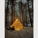 Esker tent, glowing  in a snowy forest with snowshoes near by