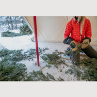Person in a red jacket sitting in front of a tent in a snowy landscape, the tent is set up using the Esker Centre Pole
