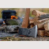 Esker Camp Axe leaning against a stack of firewood with a blurred background