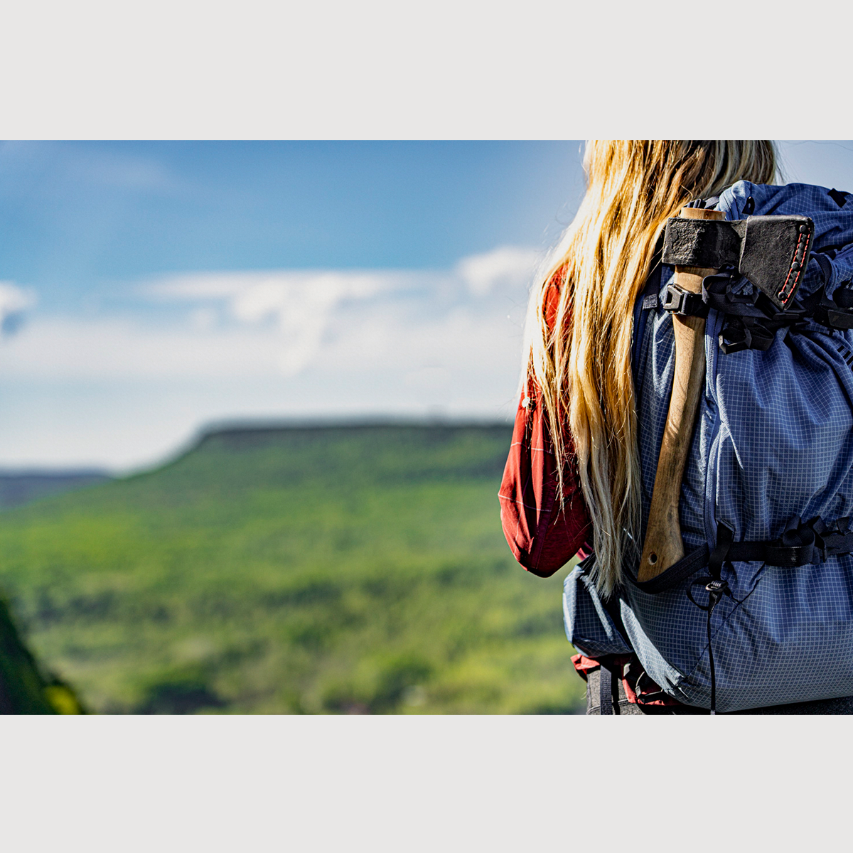 Person with an esker hatchet in their backpack looking at a scenic landscape