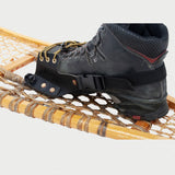 a black boot sits in an esker snowshoe binding, that is a attached to a traditional snowshoe