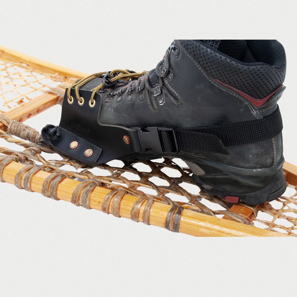 a black boot sits in an esker snowshoe binding, that is a attached to a traditional snowshoe