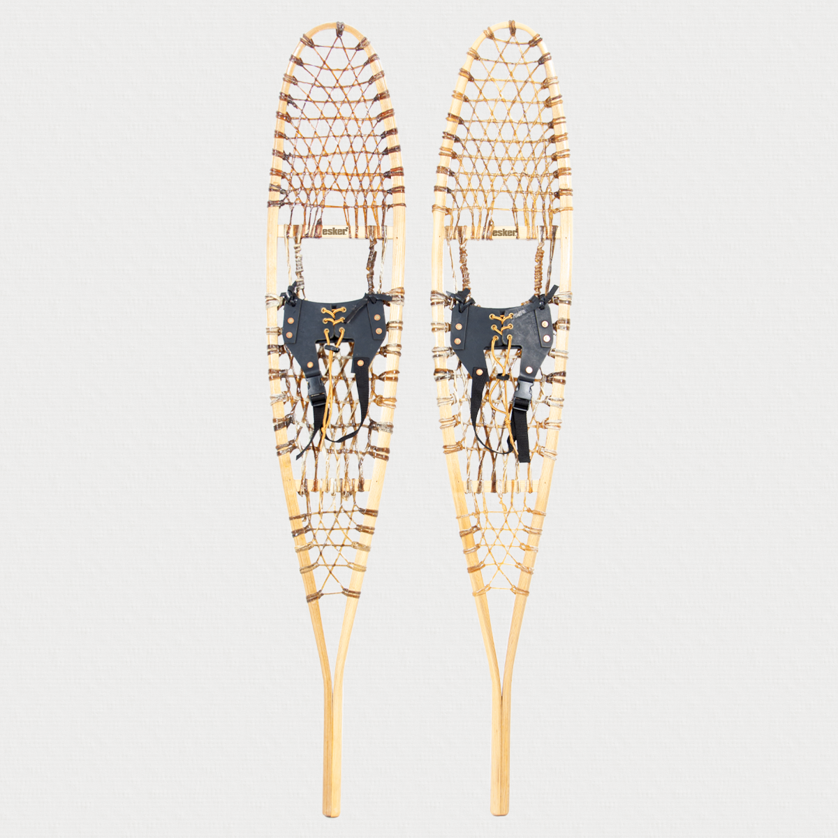 Pair of traditional snowshoes, with leather bindings on a light grey background 