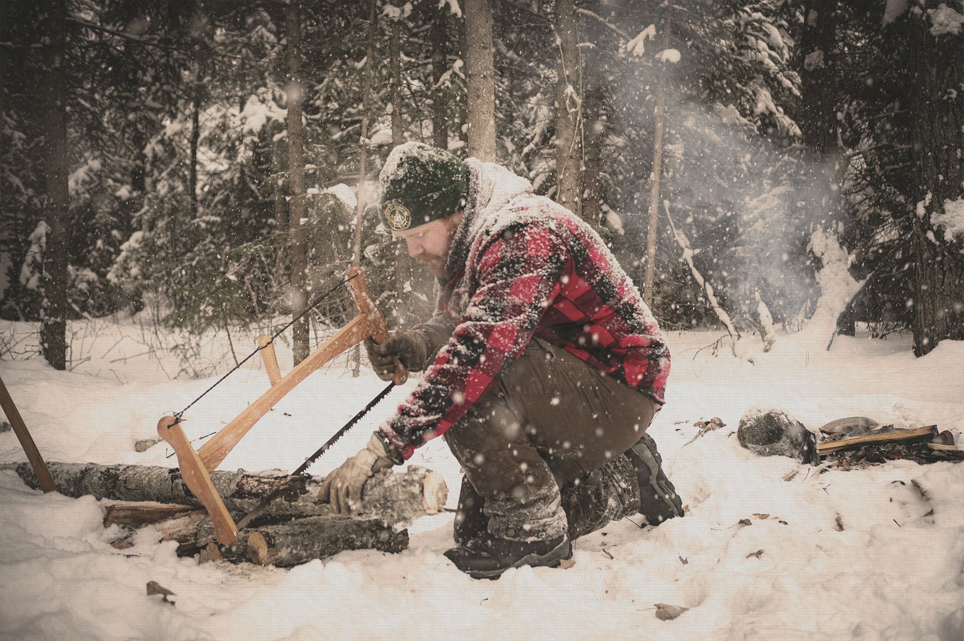 Person using a Esker bucksaw to cut wood in a snowy forest