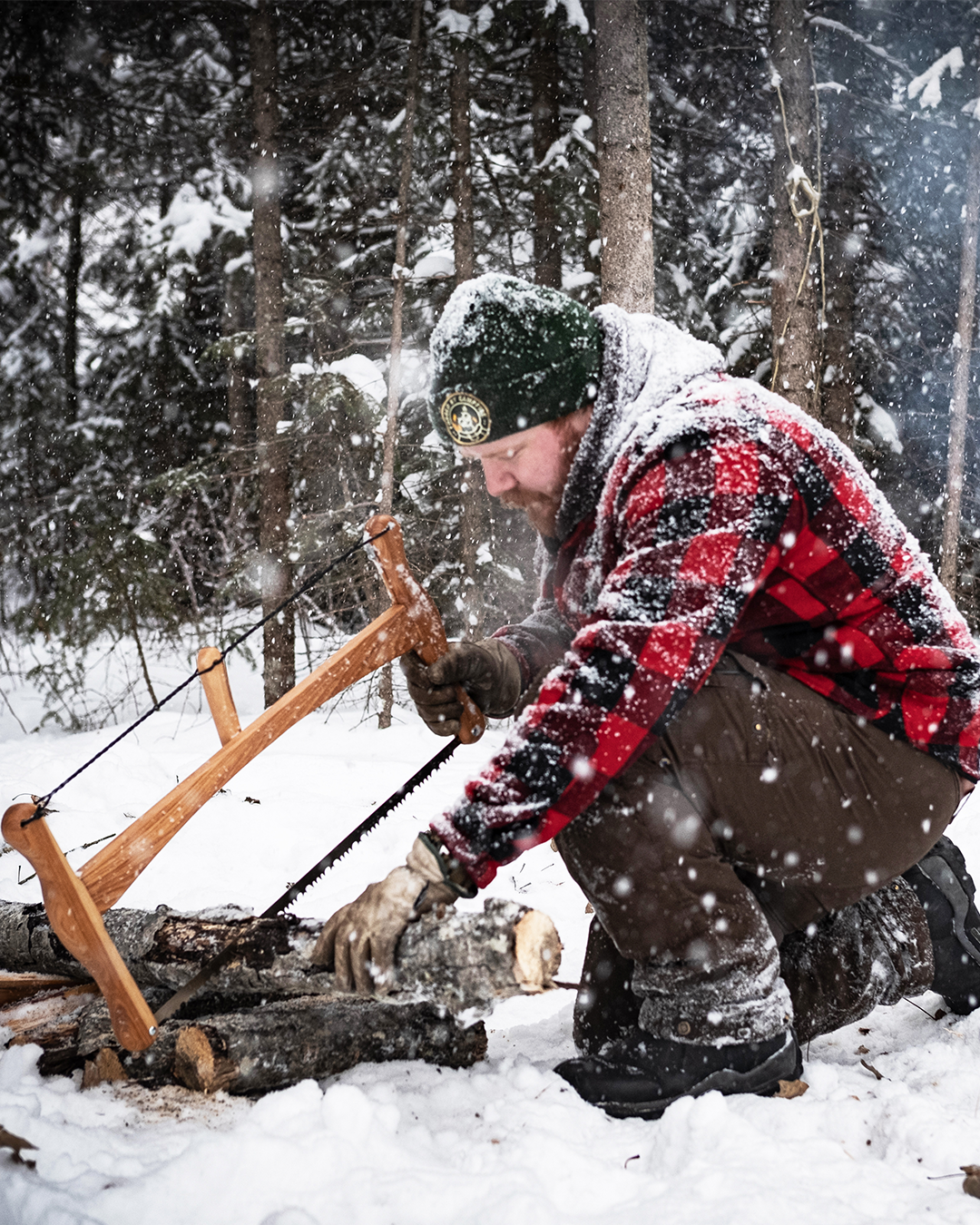 a man in a red plaid jacket cuts wood with an Esker Bucksaw